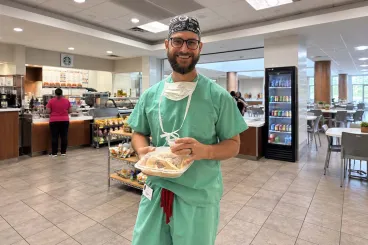 Smiling healthcare worker in green scrubs holding a prepared meal in a bright hospital cafeteria.
