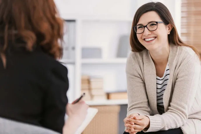 A smiling woman talks with a counselor during a one-on-one conversation in a bright, comfortable office.